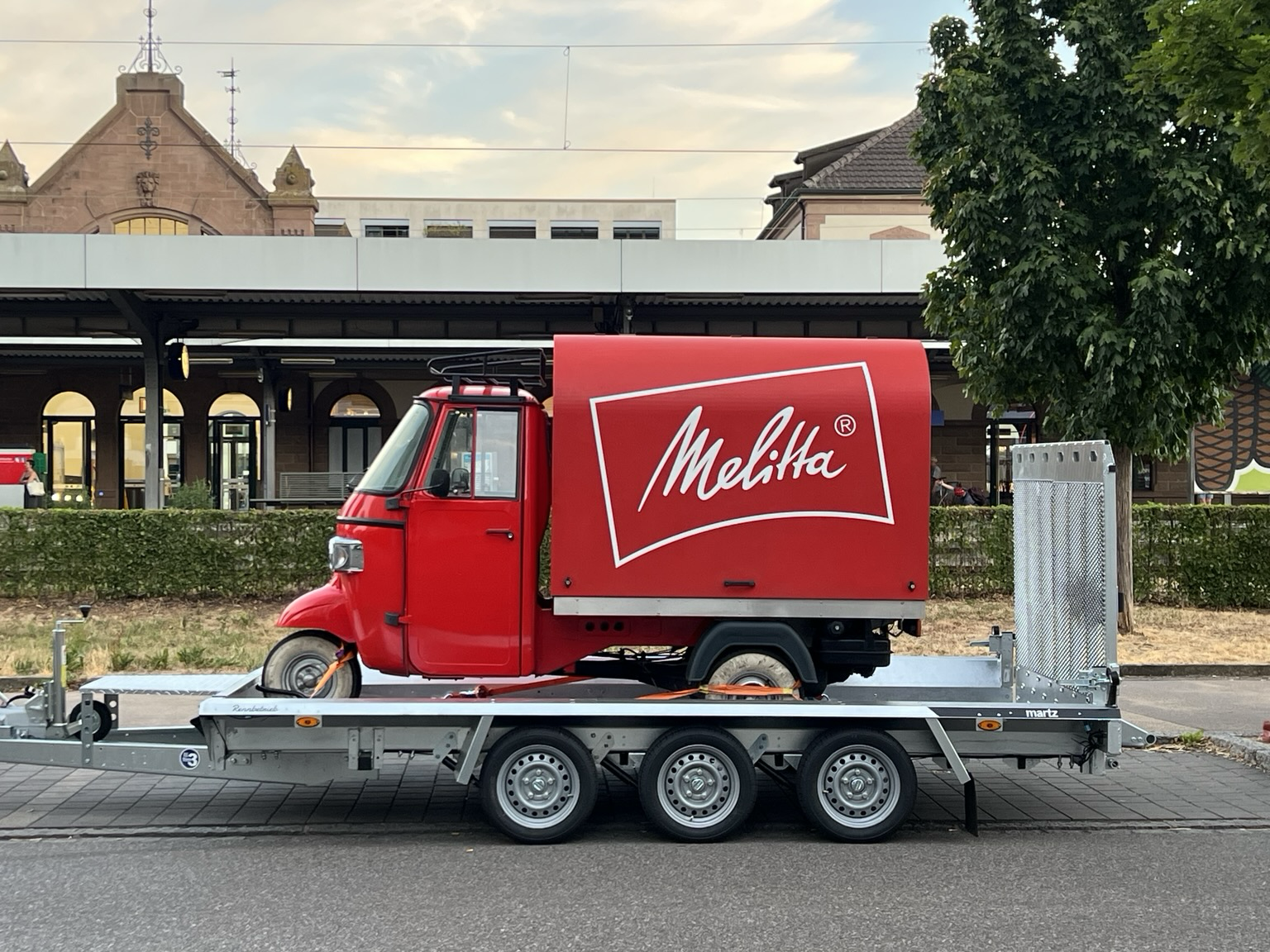 Dreirädriges Fahrzeug auf einem Anhänger. Rot mit weißer Melitta Aufschrift