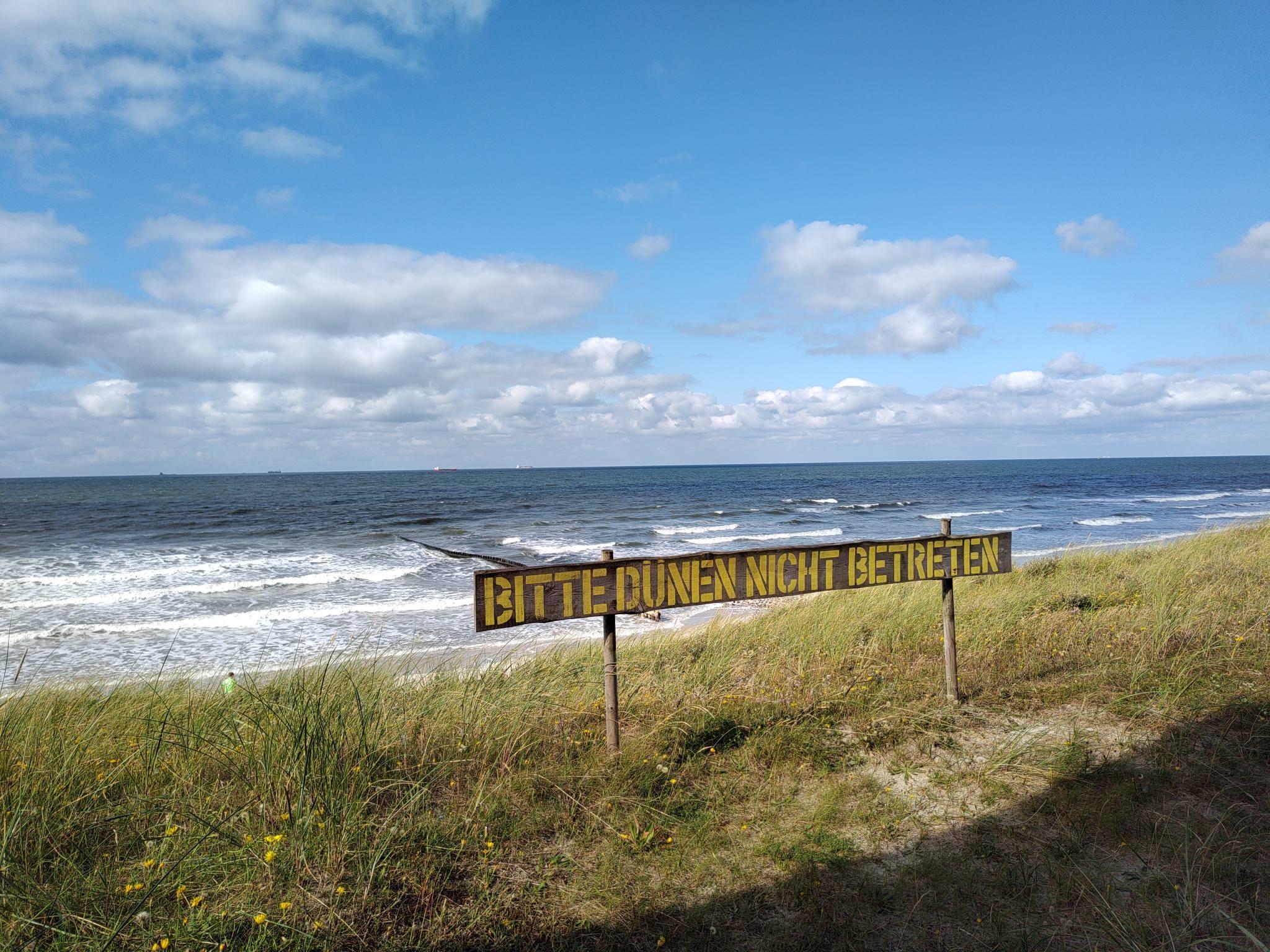 dunes and beach of Wangerooge; on the grass-overgrown dune rest a sign reading "BITTE DÜNEN NICHT BETRETEN" (PLEASE DON'T STEP ON THE DUNES)