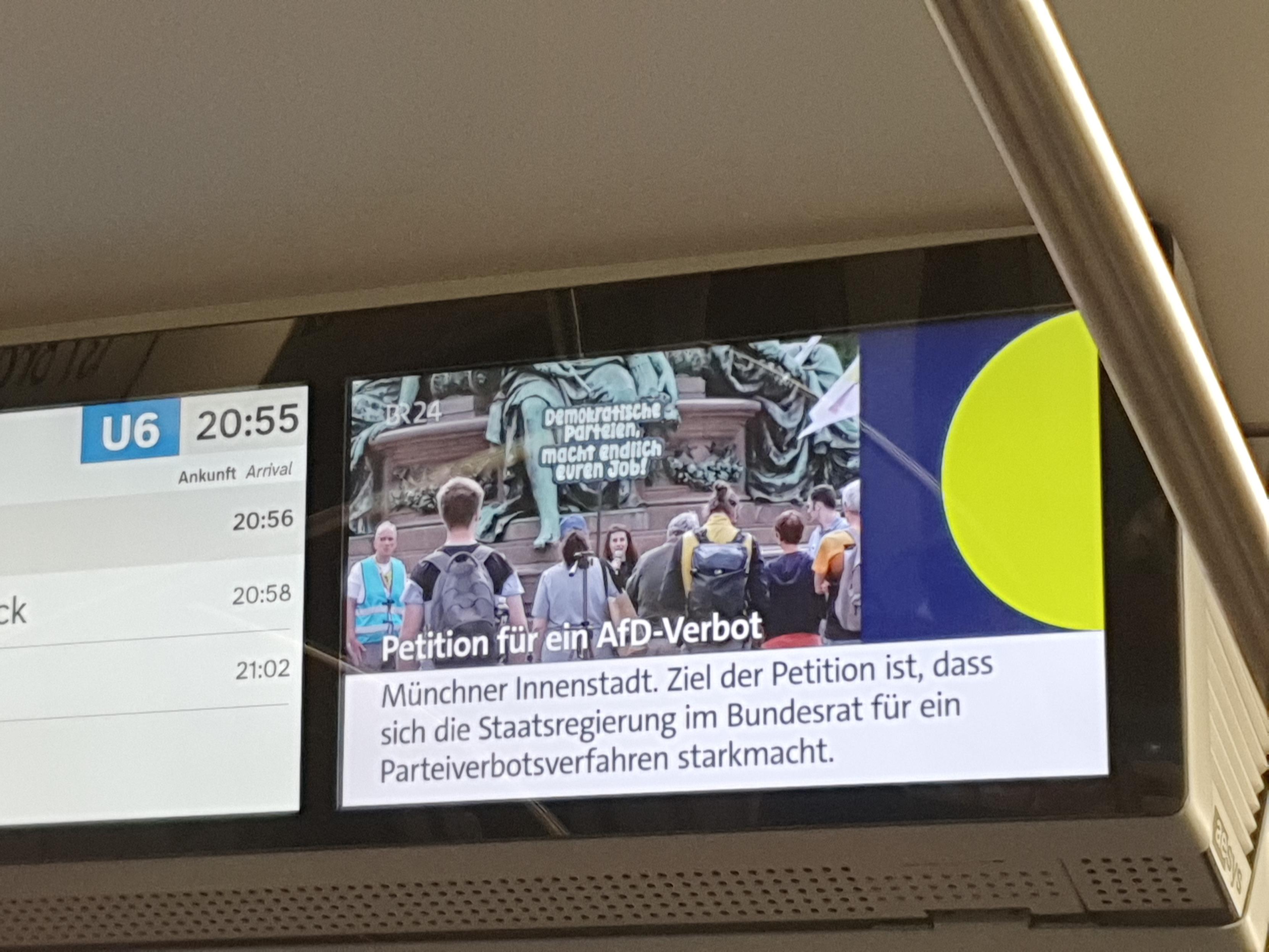 Foto vom Info-Bildschirm in der U-Bahn. Unter einem Bild von der Demo am Maxmonument vorm Landtag steht "Petition für ein AfD-Verbot. Münchner Innenstadt. Ziel der Petition ist, dass sich die Staatsregierung im Bundesrat für ein Parteiverbotsverfahren starkmacht."