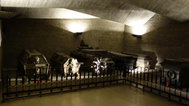 vier reichverzierte Bronzesärge nebeneinander, indirekt beleuchtet von difuusem Licht in einem Gewölbekeller einer Kirche