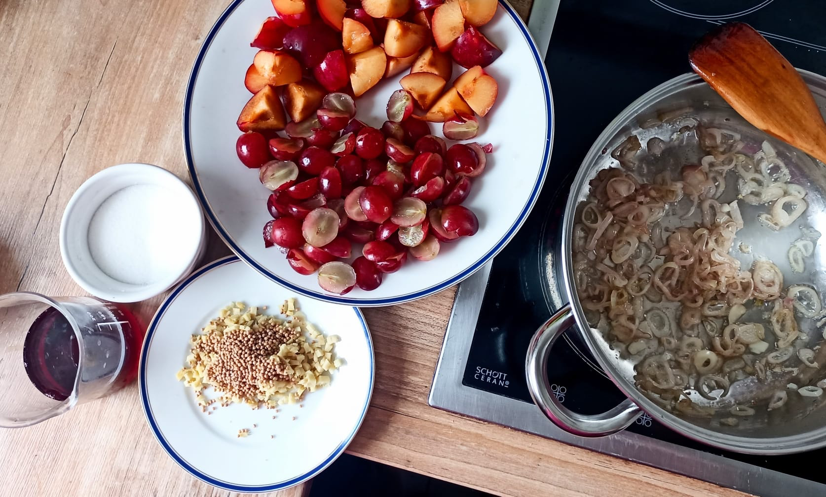 Im Topf braten die Schalotten, daneben halbierte Trauben, Pflaumen-Stücke, Zucker, gehackter Ingwer, Senfkörner + Traubensaft