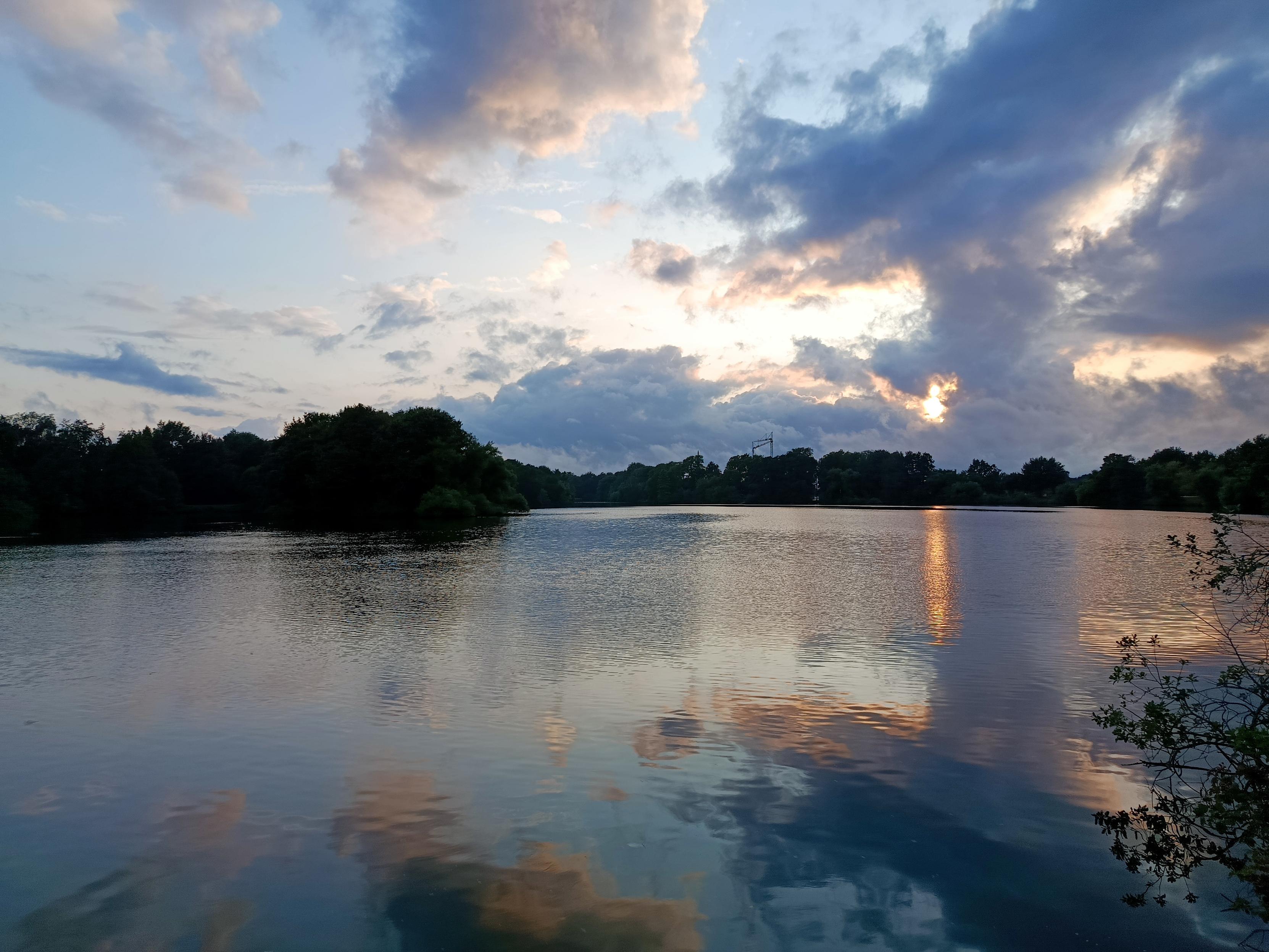 Blick über ein See mit kräftigen Wolken und Lücken die sich in ihm spiegeln