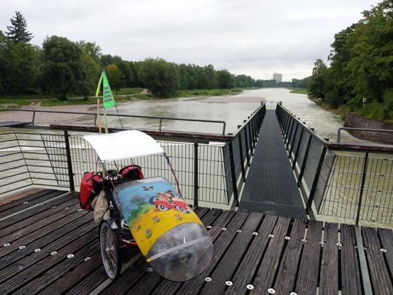 ein Liegedreirad steht auf einer Brücke über die mehr als normal volle Isar