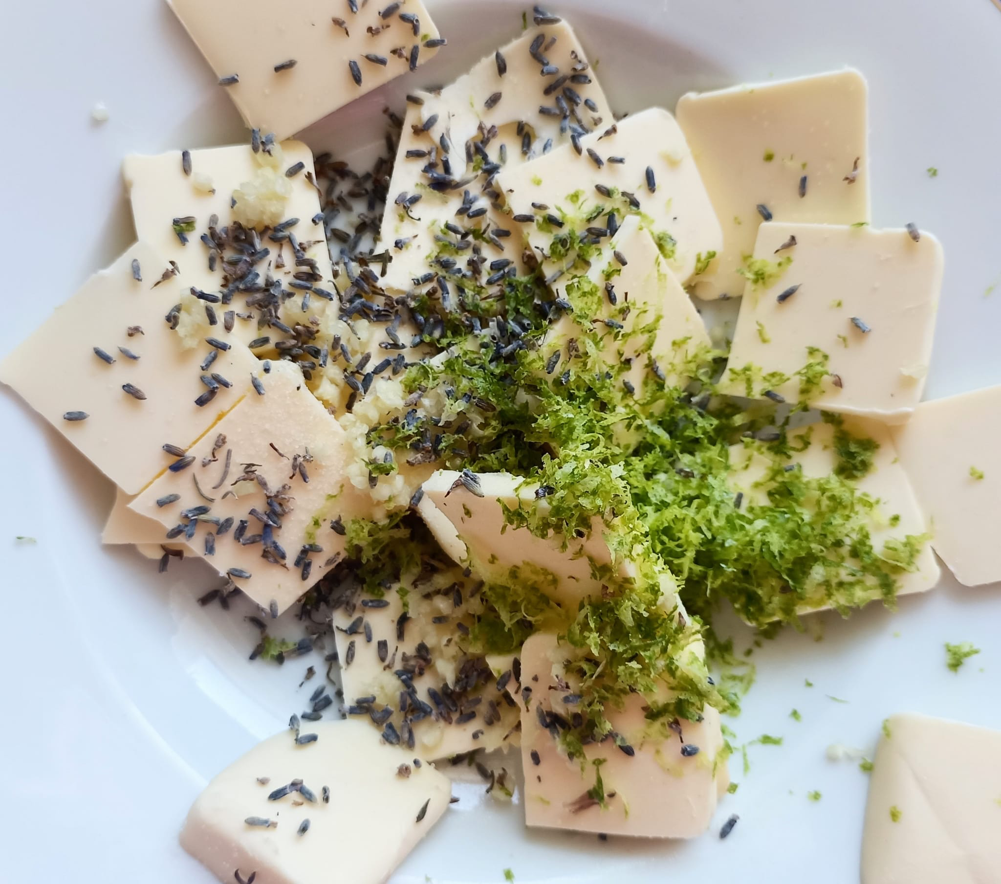 Auf einem Teller Butterstücke, Limettenabrieb, Lanendelblüten und Knoblauch