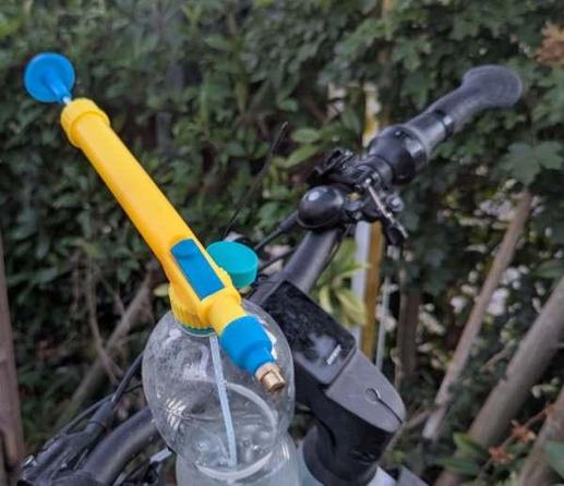 Eine PET Flasche ist mit Kabelbinder am Lenker befestigt. Ein Sprühpistolenaufsatz, der eine Pumpe und Düse hat, ersetzt den Deckel.