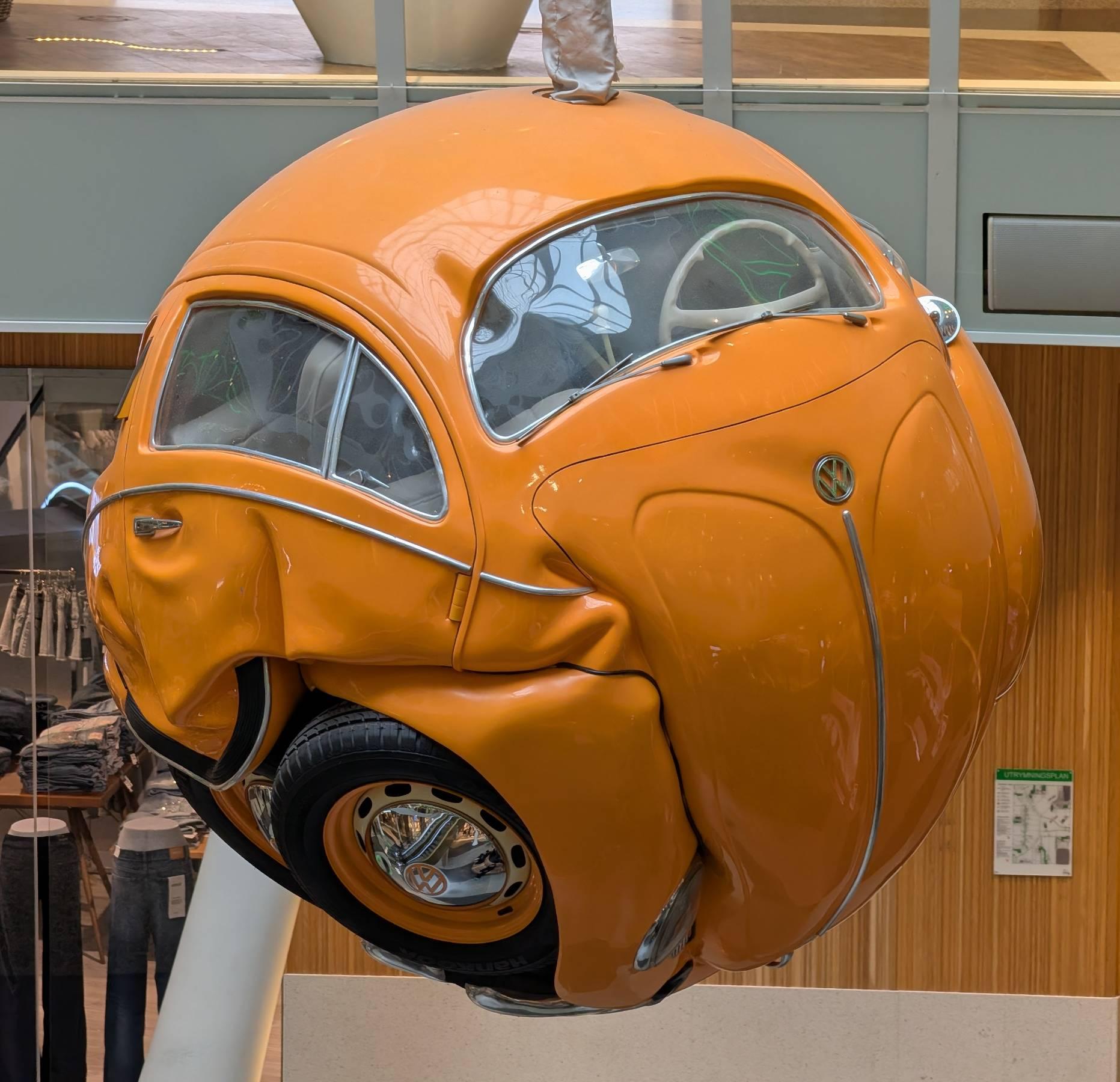 Ein oranger VW Käfer zu einer Kugel verformt.