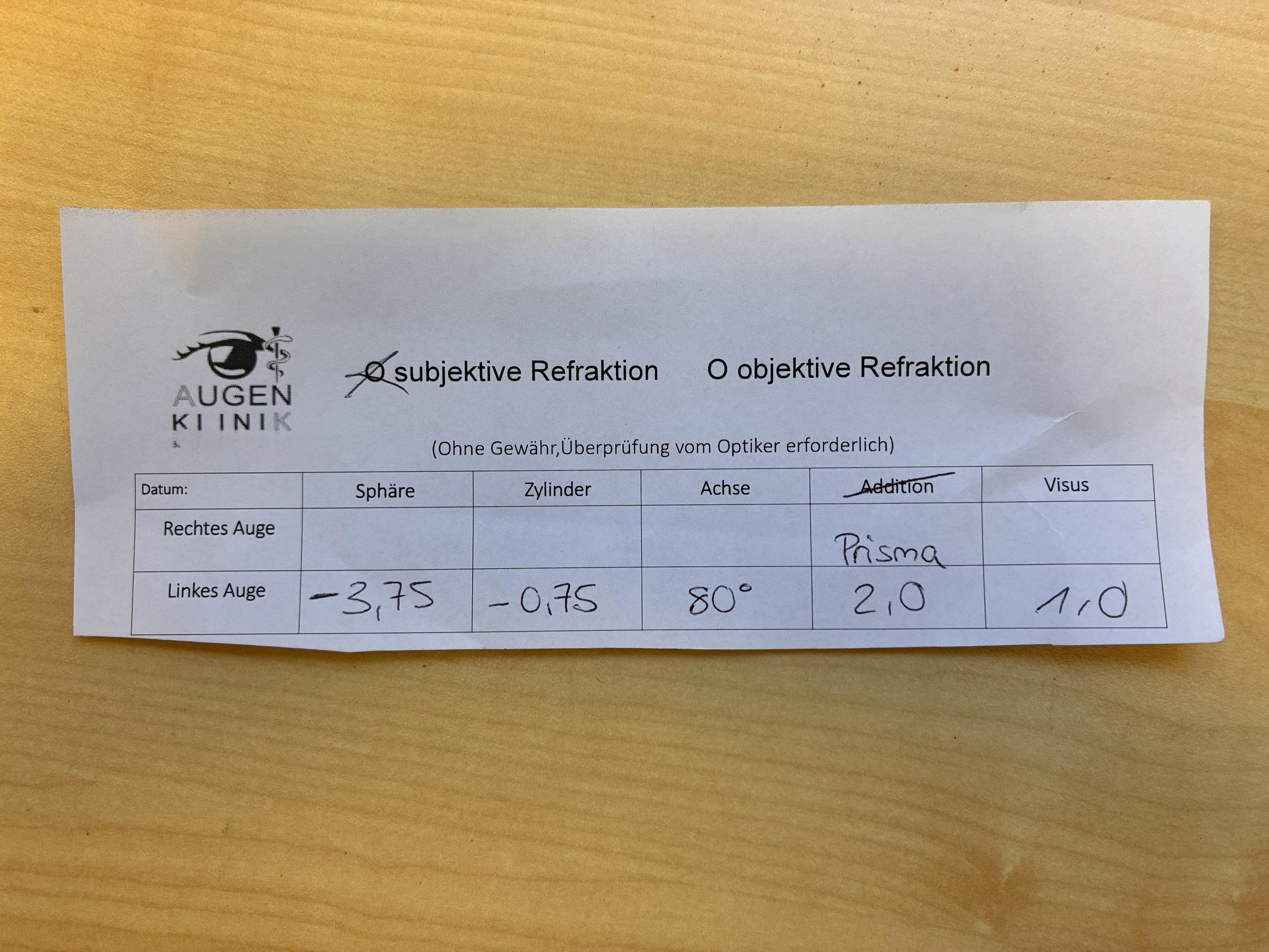 Ein Zettel, oder besser Abriss, mit einer prismatischen Brillenglasverordnung. Das rechte Glas fehlt, die Basislage des Prismas fehlt, keine Unterschrift, falsche Berufsbezeichnung für Augenoptiker. 
Den Namen der Augenklinik habe ich entfernt.
