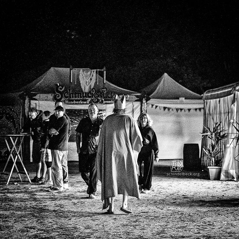 Der König macht sich auf ins Dixi-Land (ein Mann mit Umhang und Krone von hinten fotografiert in Schwarzweiss) - Fotografie von Frank Schindelbeck
