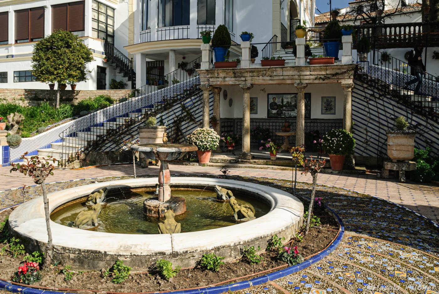 Kreisförmiger Brunnen mit Fröschen im Vordergrund. Im Hintergrund eine Treppe zum Museum.