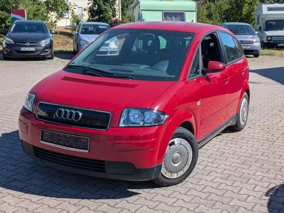 ein roter Audi A2 steht auf dem Parkplatz einer Werkstatt. Im Hintergrund ein weiterer A2