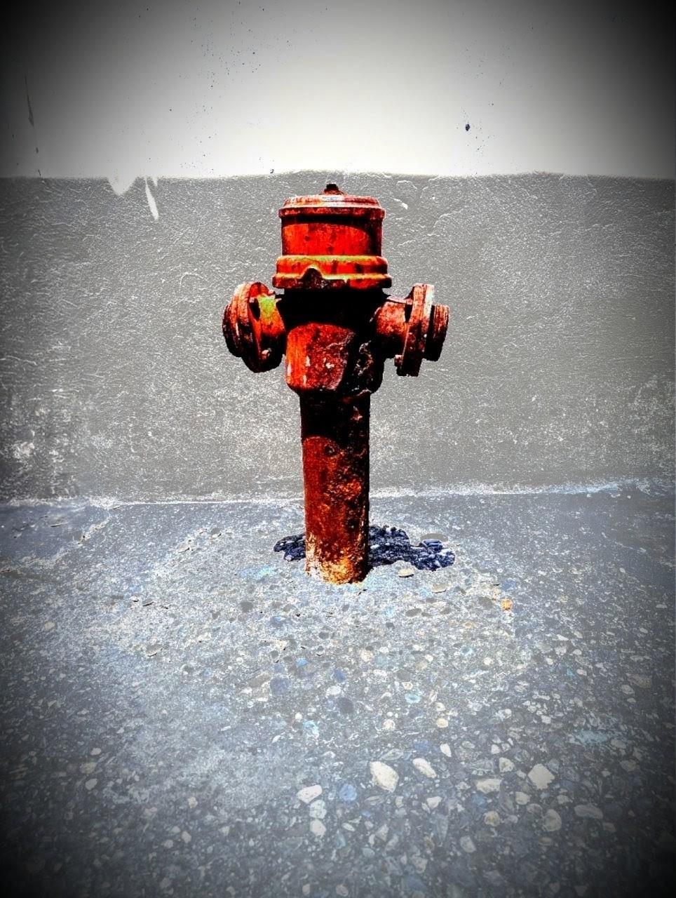 Ein altmodischer roter Hydrant aus Metall auf dem Gehweg an einer Mauer aus Beton.