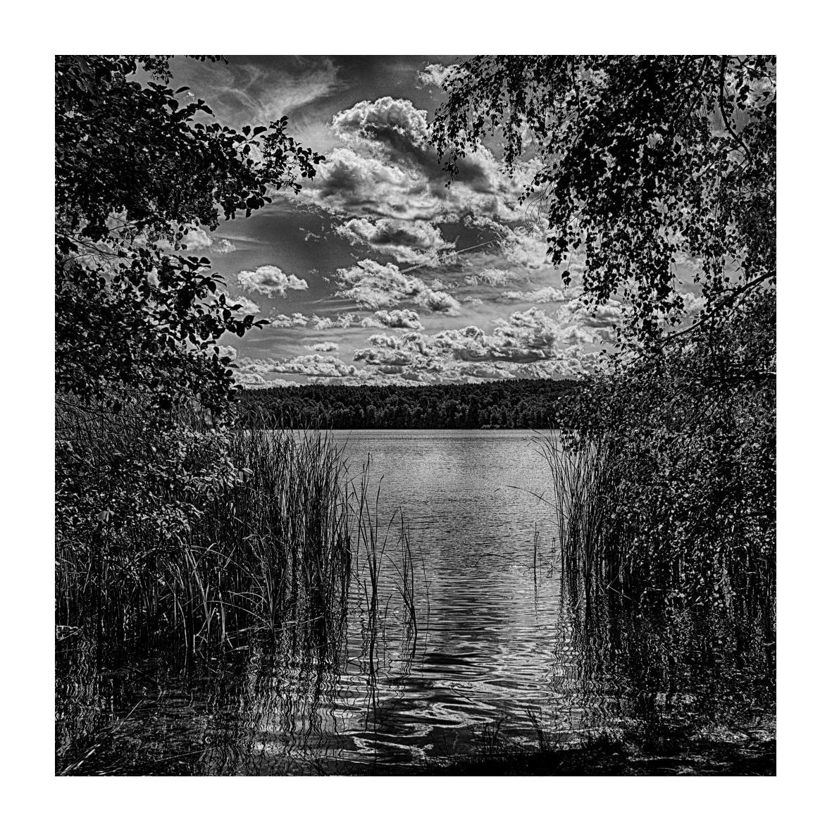 Blick durch einen schmalen Zugang auf einen See bei sonnig-bewölktem Himmel