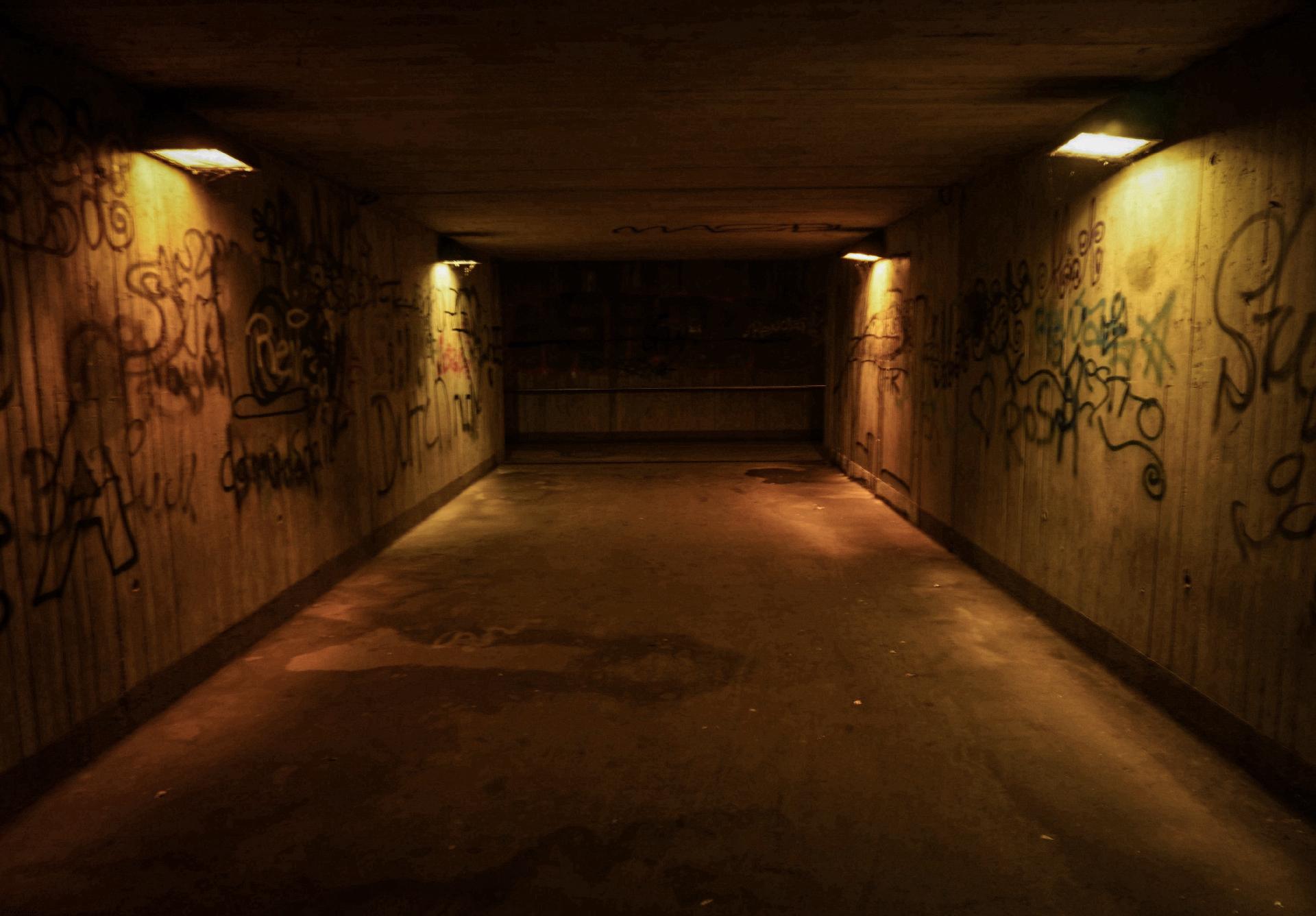 Eine erleuchtete, enge Unterführung mit vier goldgelben Lampen und Graffiti an den Wänden.