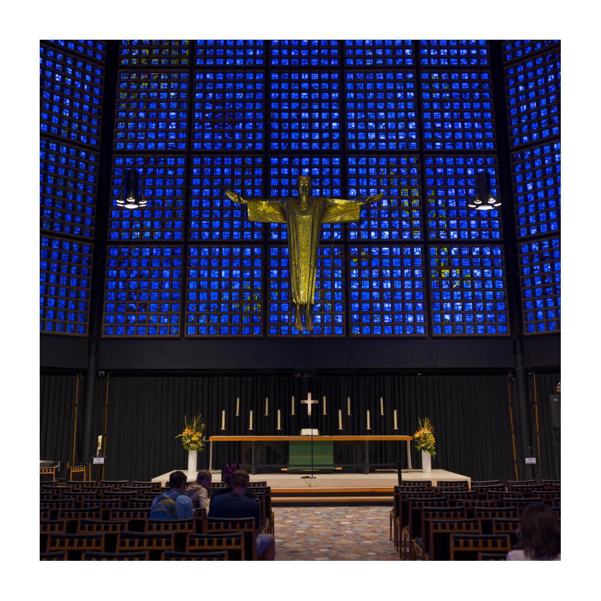 Innenraum der "Neuen Kirche" mit Altar, riesige Fensterfront aus blauen Glassteinen und einer vor der Fensterfront hängenden Jesusfigur