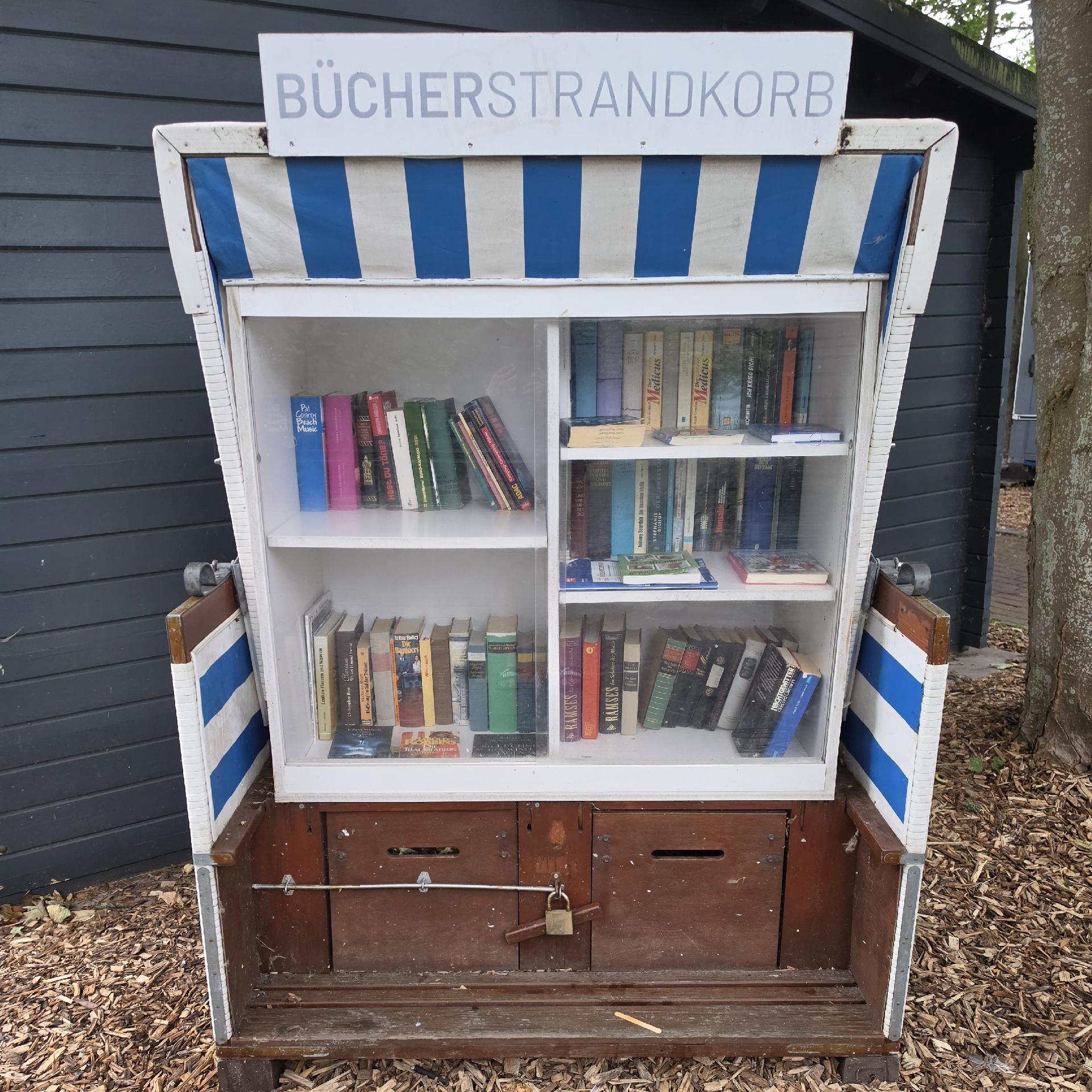 Ein Bücherschrank in Form eines blau-weiß gestreiften Strandkorbs, gefüllt mit allerlei unterschiedlichen Büchern.