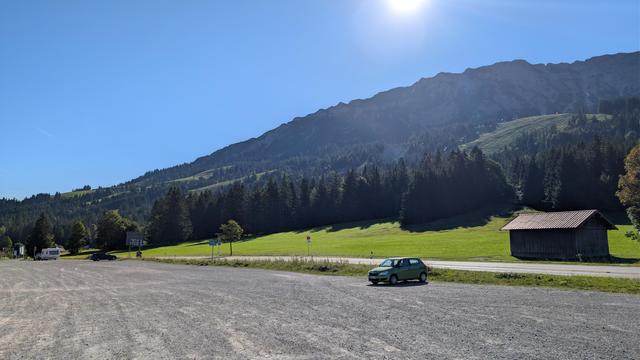 Parkplatz und bewaldeter Berg im Hintergrund, blauer Himmel gegen die Morgensonne fotografiert.