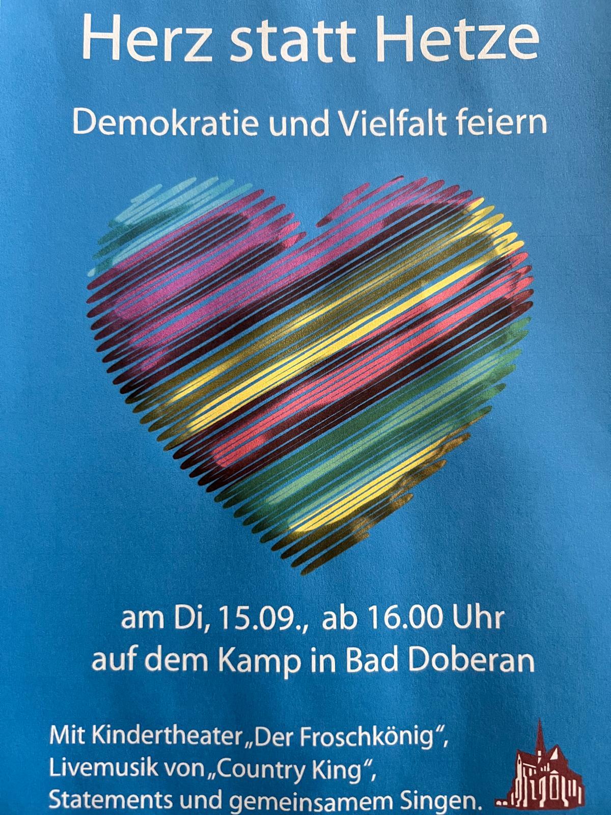 Das Bild zeigt einen Flyer mit blauem Hintergrund. Das grafische Motiv ist ein mit einem hin und her bewegtem Pinselstrich gemaltes buntes Herz. 
In weißer Schrift steht über dem Herz:
"Hert statt Hetze" - "Demokratie und Vielfalt feiern"
Unter dem Herz die Angaben:
"am Di, 15.09., ab 16.00 Uhr auf dem Kamp in Bad Doberan"
Ganz unten:
"Mit Kindertheater 'Der Froschkönig', LiveMusik von 'Country King', Statements und gemeinsamem Singen."
Rechts unten ein Logo, das das Münster darstellt.
