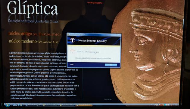 Bild eines Bildschirms das Windows 7 Desktop, auf dem Norton Security aufgepoppt ist. Rechts auf dem Bidlschrim sieht man eine antike Scheibe mit einem Portrait in Seitenansicht aus Ton.