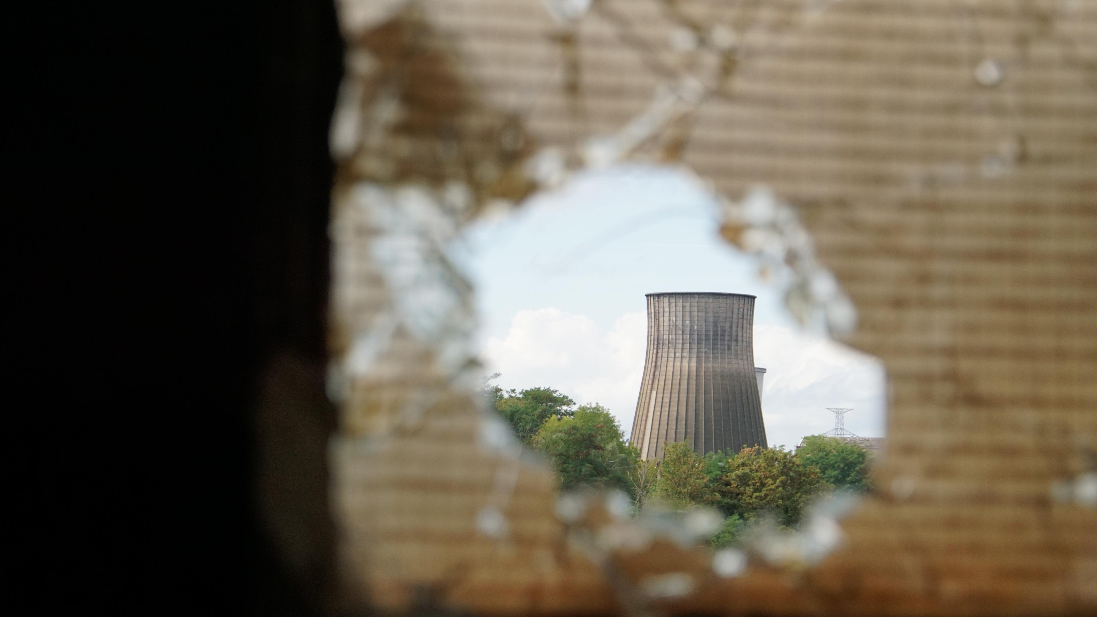 Durche ein Loch in einer dreckigen Sicherheitsglasscheibe ist ein Kühlturm zu sehen