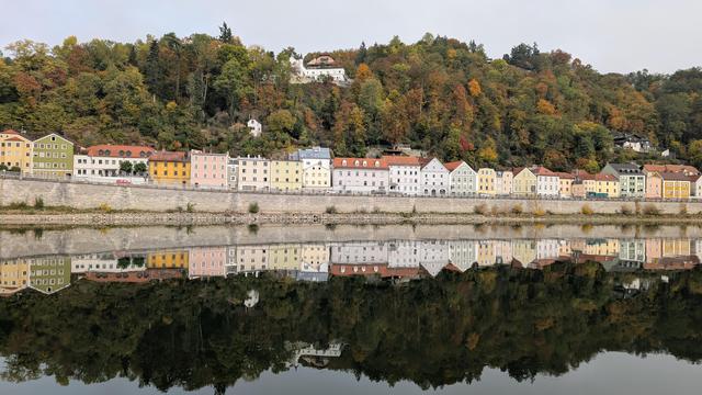 Häuserfassaden in Passau auf der anderen Seite der Donau gelegen als die Altstadt auf der Insel. Die Häuserfassade mit ihren bunten Farben spiegelt sich detailgetreu in der Donau. Dahinter Wald in herbstlichen Farben.