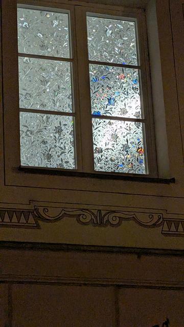Fenster in der Dunkelheit, von innen hell erleuchtet zeigt die bunten Blüten der von innen angebrachten Klebefolie an.